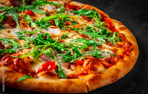 Pizza with chicken, bacon, cheese, tomato and arugula. Italian pizza on Dark grey black slate background