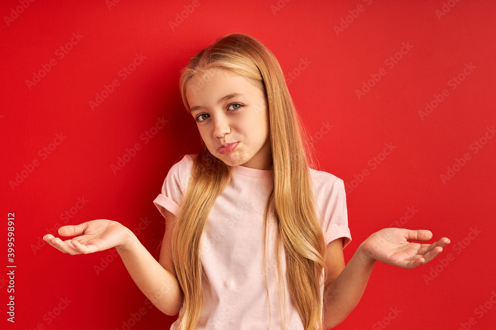 I don't know. misunderstanding little girl shrugging at camera, caucasian child in casual t-shirt posing isolated on red background
