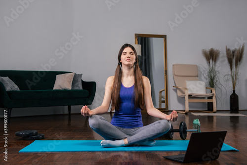 Young woman doing yoga exercises at home in a modern liiving room while watching online video lesson