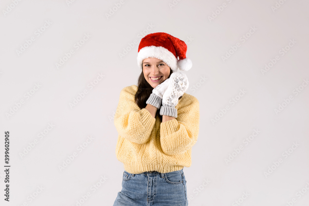 Beautiful young woman in Santa red hat and white mittens smiling looking in to the camera isolated on white background Beautiful young woman in Santa red hat and white mittens smiling looking in to the camera isolated on white background