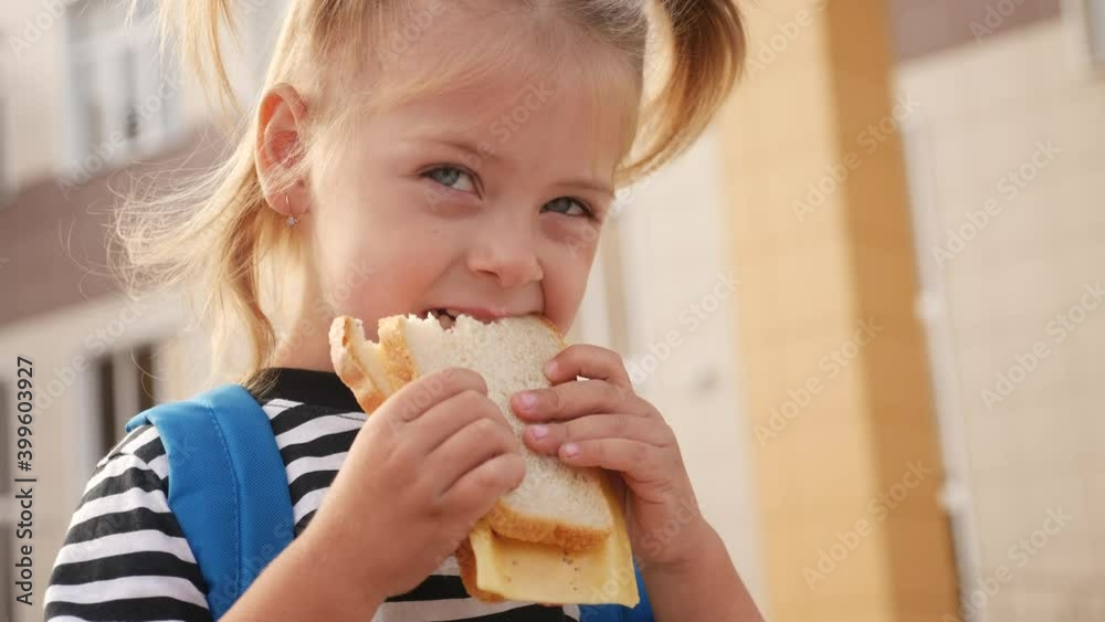 schoolgirl eating a sandwich during recess in school. kids education concept lifestyle. little girl kid schoolgirl with a backpack eating a sandwich. kid child is having lunch at school schoolgirl eating a sandwich during recess in school. kids education concept lifestyle. little girl kid schoolgirl with a backpack eating a sandwich. kid child is having lunch at school