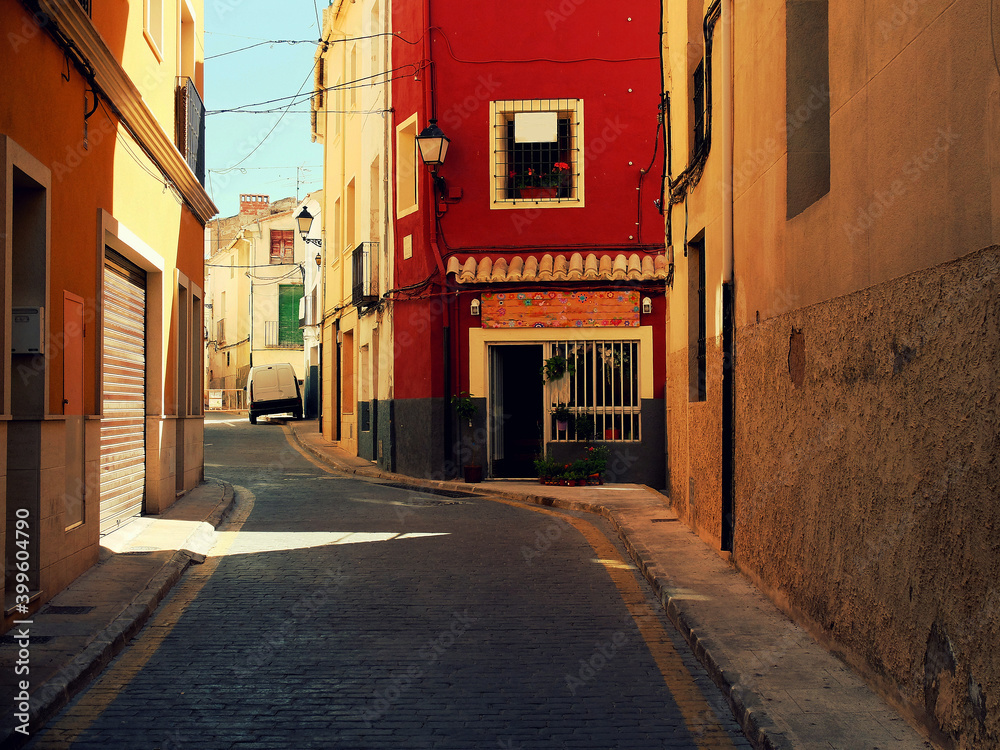The colorful world of Spain. Red and yellow buildings. The street is going uphill. Blue sky.
