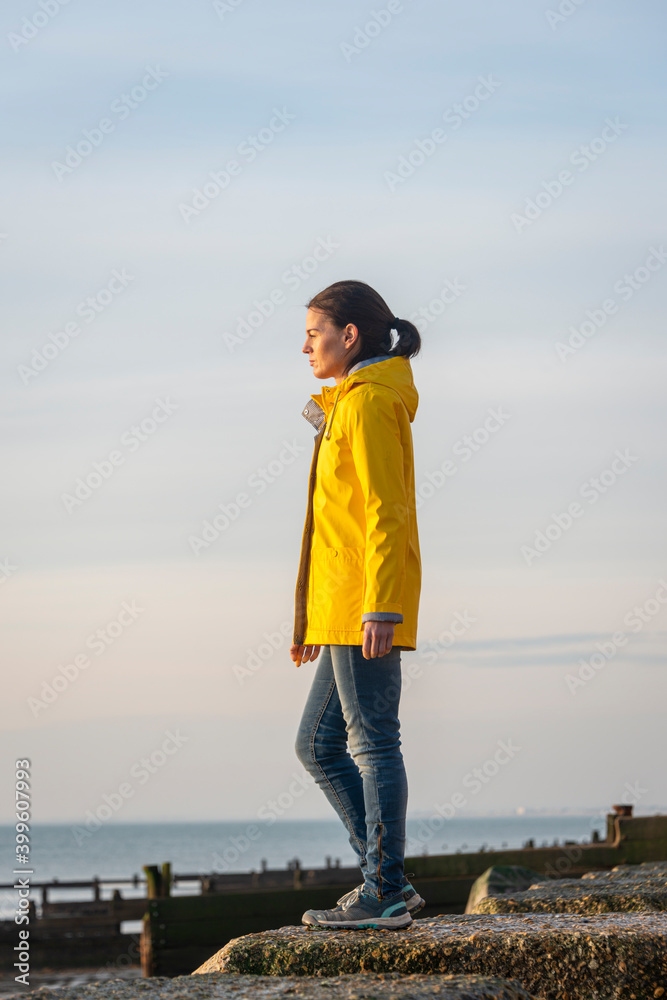 Mature woman wearing a yellow jacket, looking out to sea. Alone concept.
