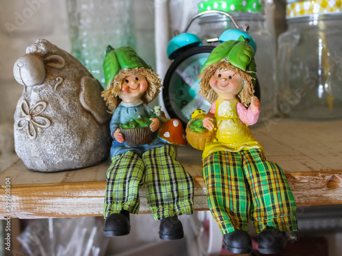 Two ceramic dolls sitting on a wooden shelf, plaid trousers