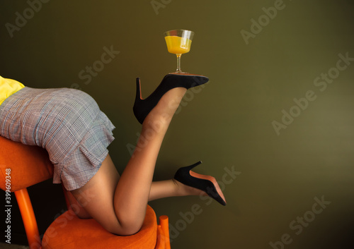 Sexy woman balances a glass with a cocktail on his leg on the green wall, creative photo