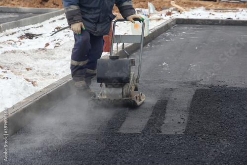 Worker use vibratory plate compactor for ramming asphalt. Men at work. Laying new asphalt pavement on the road.