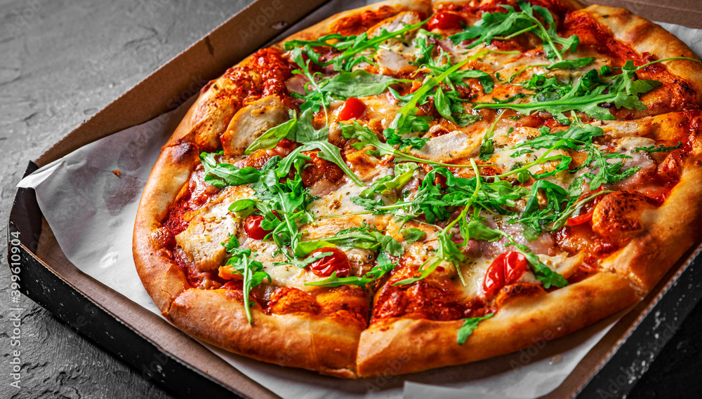 Pizza with chicken, bacon, cheese, tomato and arugula in paper box. Italian pizza on Dark grey black slate background