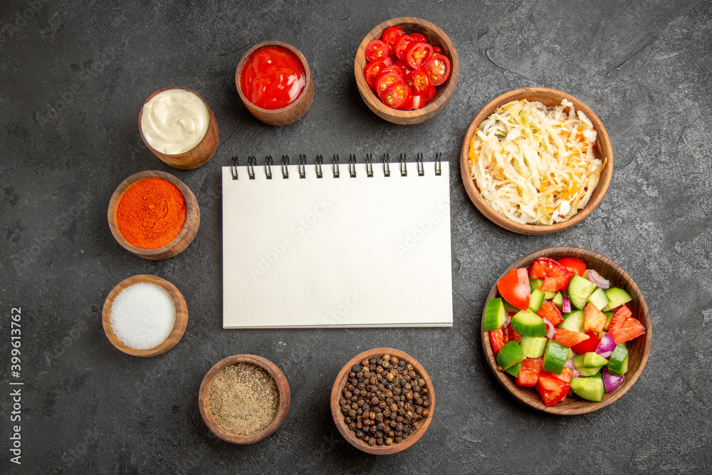 Top view of different spices sauerkraut salad mayonnaise and ketchup around notebook on dark table