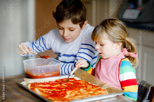 Two siblings  little children making italian pizza at home. Cute toddler girl and school boy having fun in home kitchen  indoors. Brother and sister  family helping and preparing meal
