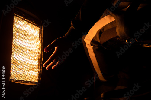 Closeup hand of a man using halogen heater to keep warm in winter isolated in black background.
