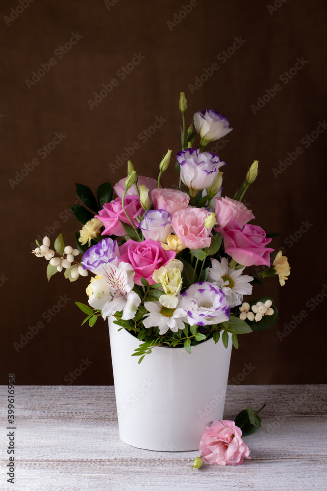 a luxurious bouquet of roses, daisies, chrysanthemums, unopened buds in a white round box, a sprig of lisianthus on a gray table and a background of burlap. a luxurious bouquet of roses, daisies, chrysanthemums, unopened buds in a white round box, a sprig of lisianthus on a gray table and a background of burlap.