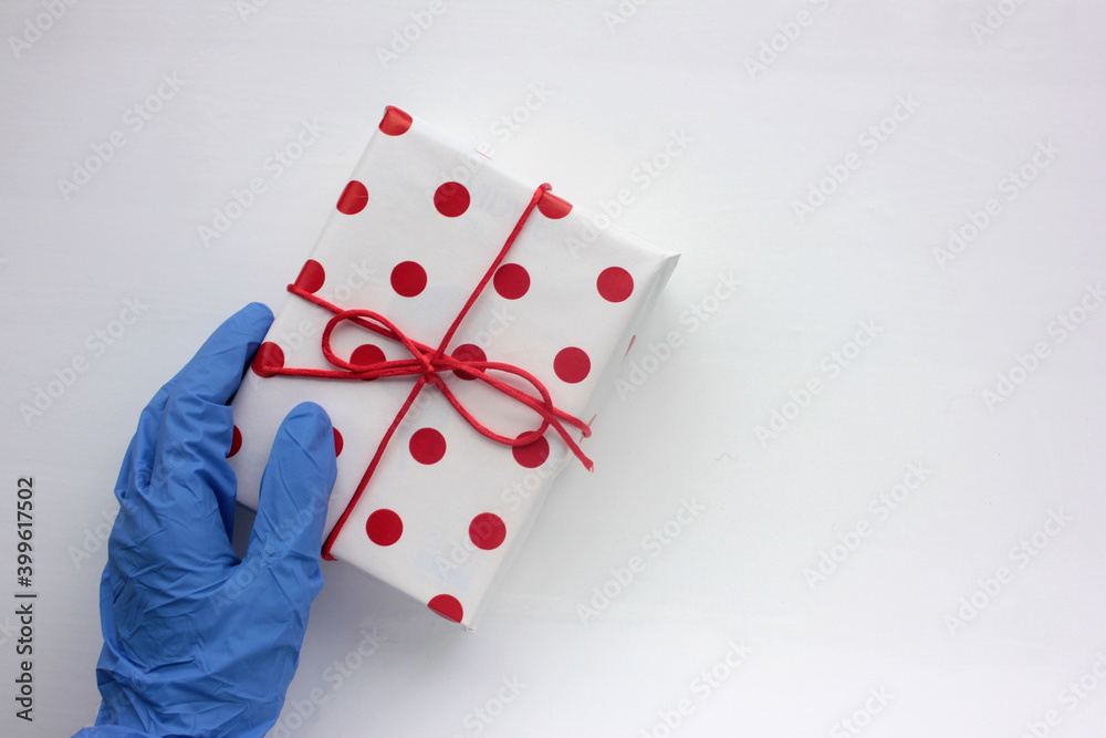 Hand in medical glove with a present. Overhead view of wrapped gift box with red ribbon on white background. Hand in medical glove with a present. Overhead view of wrapped gift box with red ribbon on white background.