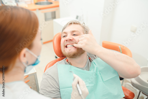 A man sits in the dentist's chair and points his finger at the doctor with a sore tooth. Dentistry concept, teeth and gum health