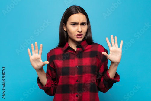 young hispanic woman feeling stupefied and scared, fearing something frightening, with hands open up front saying stay away photo