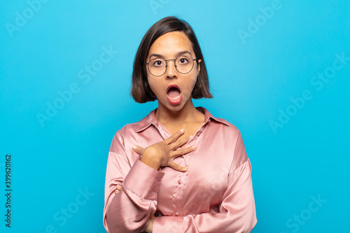 young hispanic woman feeling shocked, astonished and surprised, with hand on chest and open mouth, saying who, me? photo