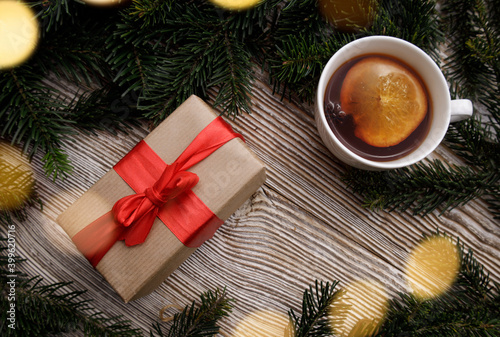 gift box with a red bow and a cup with a fragrant hot drink with fruit stands on a wooden table between fir branches. concept for Christmas and New Year holidays.light bulbs garlands around
