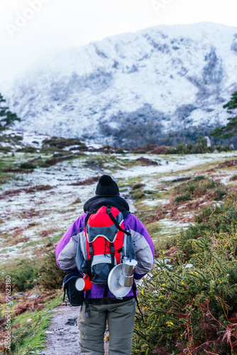 Unrecognizable hiker carrying a backpack and ascending a snowy mountain in winter. vertical stock image. camping utensils.