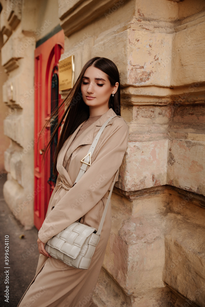 charming brunette with beige coat stands against a beautiful wall. girl in a beret. classic clothes, amazing style