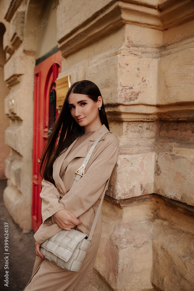 charming brunette with beige coat stands against a beautiful wall. girl in a beret. classic clothes, amazing style charming brunette with beige coat stands against a beautiful wall. girl in a beret. classic clothes, amazing style