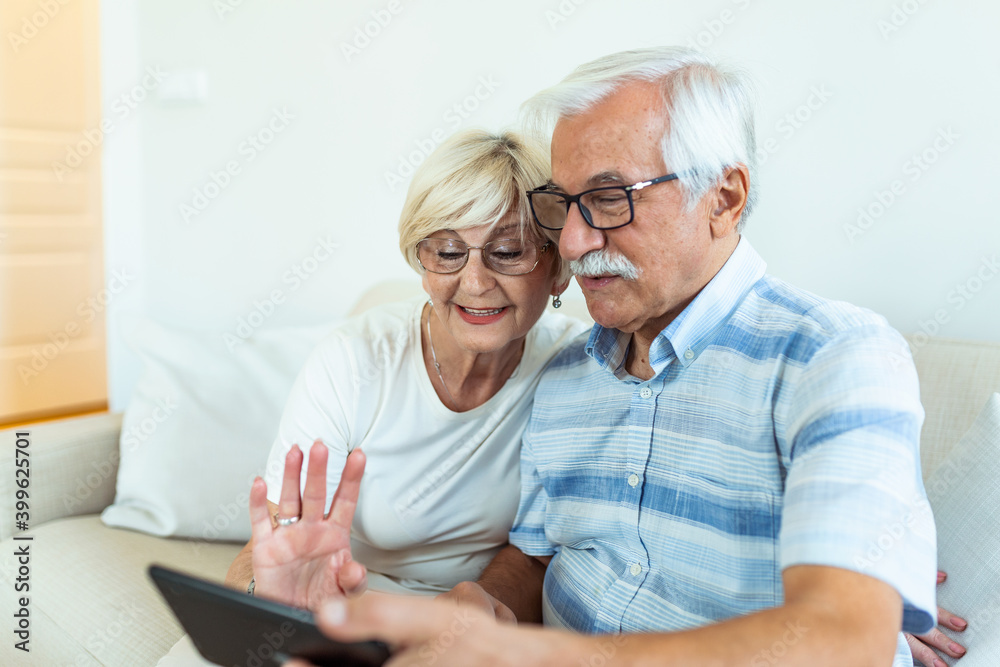 Couple of seniors smiling and looking at the same tablet hugged on the sofa - indoor, at home concept - caucasians mature and retired man and woman using technology