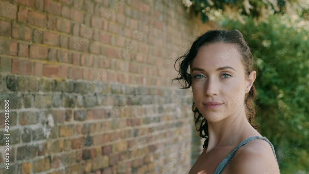 Woman standing by a brick wall while looking straight at the camera and smiling Woman standing by a brick wall while looking straight at the camera and smiling