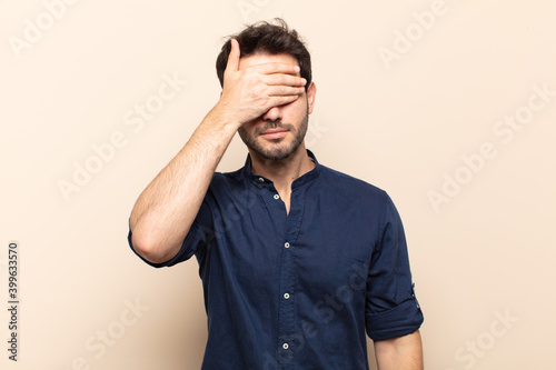 young handsome man covering eyes with one hand feeling scared or anxious, wondering or blindly waiting for a surprise photo