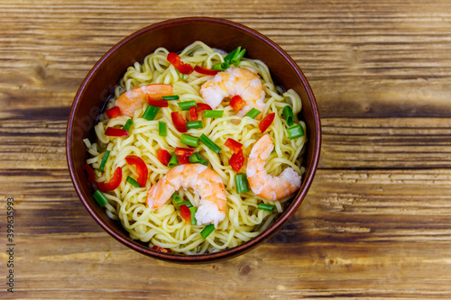 Bowl of instant Chinese noodles with shrimps, green onion and red hot chilli peppers on wooden table. Top view