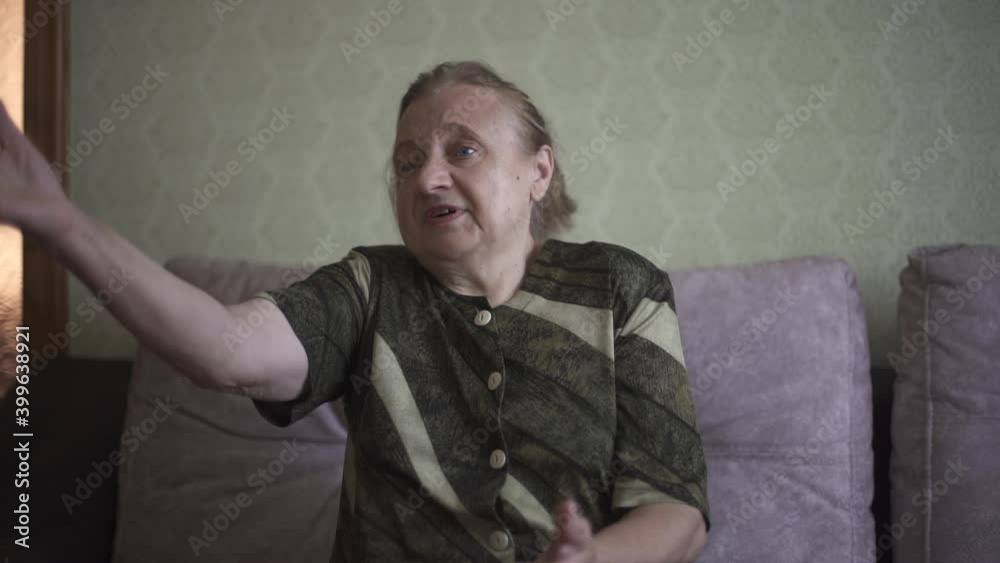 Grandmother tells a story emotionally. Retiree explains something to someone emotionally and uses a hand gestures. Elderly woman is having an emotional conversation in her living room. High quality Grandmother tells a story emotionally. Retiree explains something to someone emotionally and uses a hand gestures. Elderly woman is having an emotional conversation in her living room. High quality