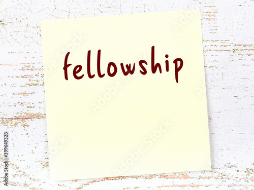 Fototapeta Yellow sticky note on wooden wall with handwritten word fellowship