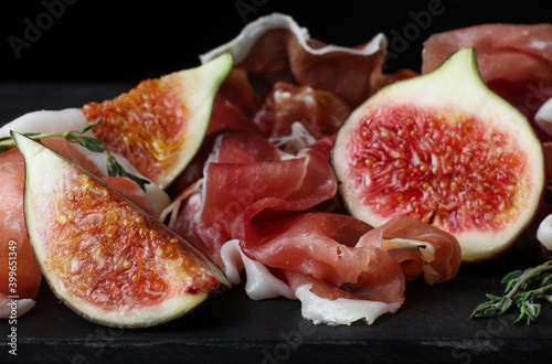 Delicious ripe figs and prosciutto served on slate board, closeup