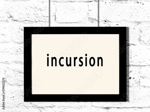 Black frame hanging on white brick wall with inscription incursion