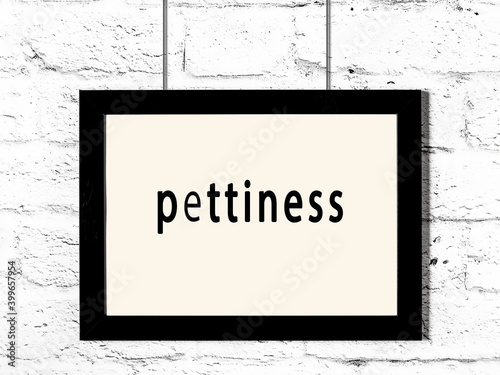 Black frame hanging on white brick wall with inscription pettiness