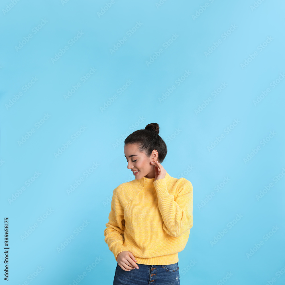 Beautiful young woman wearing yellow warm sweater on light blue background. Space for text Beautiful young woman wearing yellow warm sweater on light blue background. Space for text