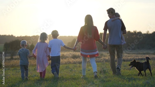 A large friendly family walks across the field at sunset with dog.