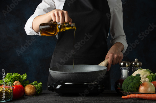Foto Professional chef pours olive oil into frying pan for cooking soup on dark blue background
