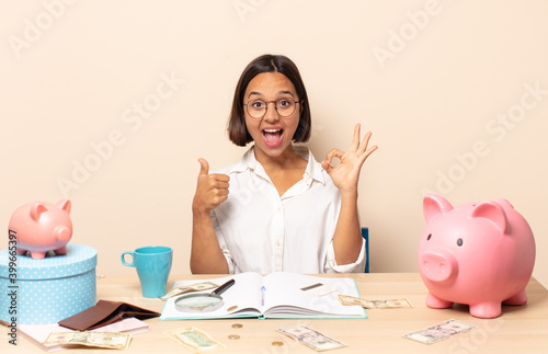 young latin woman feeling happy, amazed, satisfied and surprised, showing okay and thumbs up gestures, smiling photo