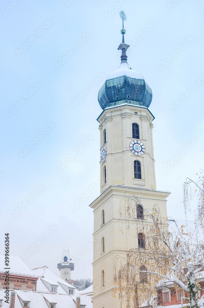 The Franciscan Church tower and the famous clock tower in the background, in the city center of Graz, Styria region, Austria, with snow, in winter