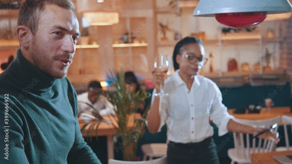 Young man holding her drunk afro-american funny girlfriend drinking lots of wine while staying in the cafe. Alcoholic woman. Humor concept.