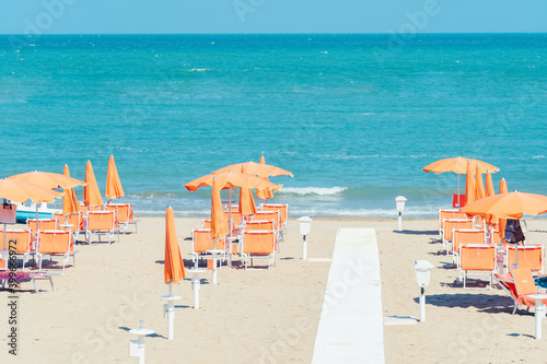 Sunbeds and parasols on the seashore. Beach, sea and umbrellas on summer day. Adriatic coast, Rimini, Italy, view from Gabicce Mare. photo