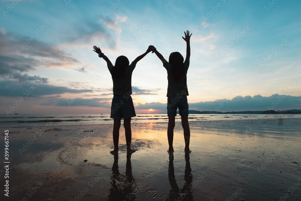 Fototapeta premium Silhouette of two asian child girls playing on the beach together at the sunset time with beautiful sea and sky. Family enjoy with nature concept.