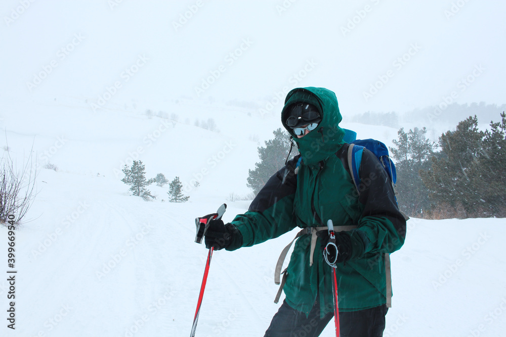 Winter hiking in the mountains. Active lifestyle concept. A hiker in equipment for winter mountain hiking and active sports. Membrane jacket, sports goggles, trekking poles