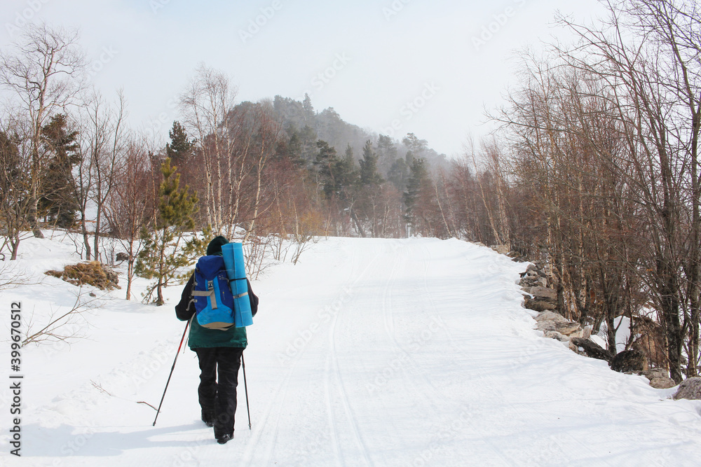 Camping in the winter season. Trekking in the mountains in winter. Active lifestyle. Sports at any time of the year. Mountaineer walk on snow path on forest with trekking pole