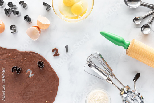 Top down view of a baking scene with baking utensils, ingredients and number cookie cutters using 2021.