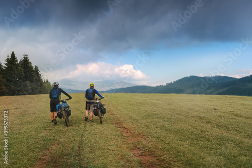 Two cyclists pushing their bicycles with baggage up a muddy meadow in the mountains. photo