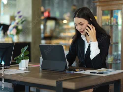 Businesswoman talking on the phone while working with tablet in cafe