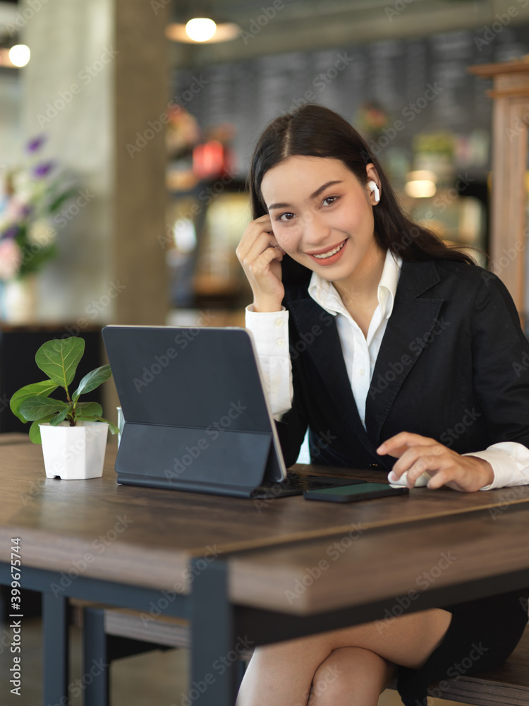 Businesswoman with earphone smiling to camera while working with tablet and smartphone Businesswoman with earphone smiling to camera while working with tablet and smartphone