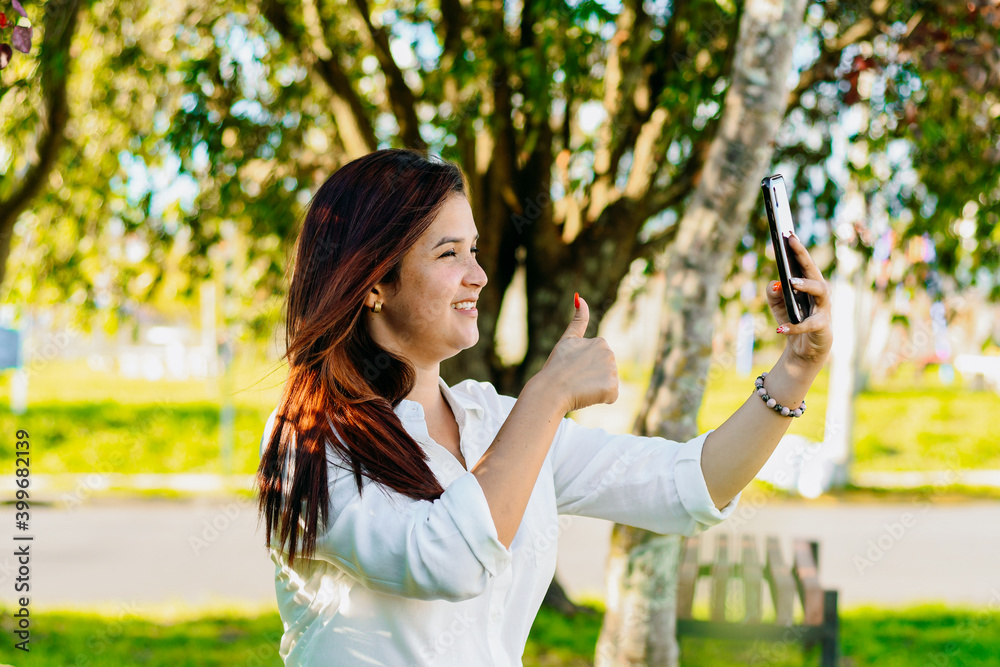 Executive woman making a video call, sitting in the park. Making a sign of everything well with her hand. Executive woman making a video call, sitting in the park. Making a sign of everything well with her hand.