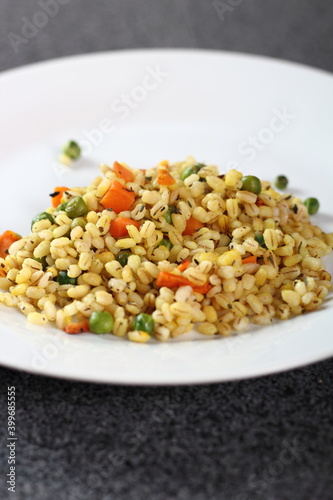 Cooked pearl barley with carrot and green peas on plate