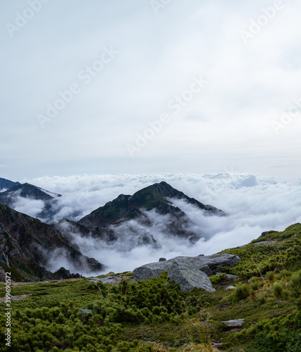 View of Kiso Mountains Range engulfed in thick clouds in the background with rock formations on grassland in the foreground in early autumn at Senjojiki Cirque in Nagano Prefecture, Japan.
