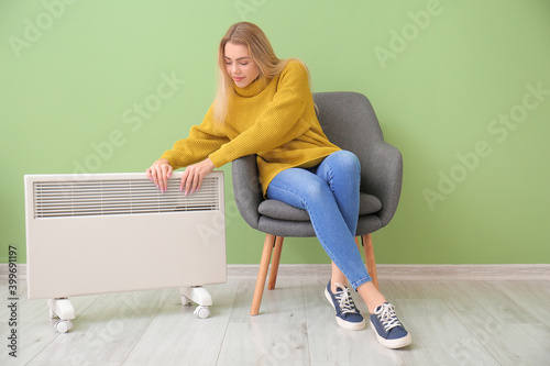 Young woman warming hands near electric heater. Concept of heating season photo